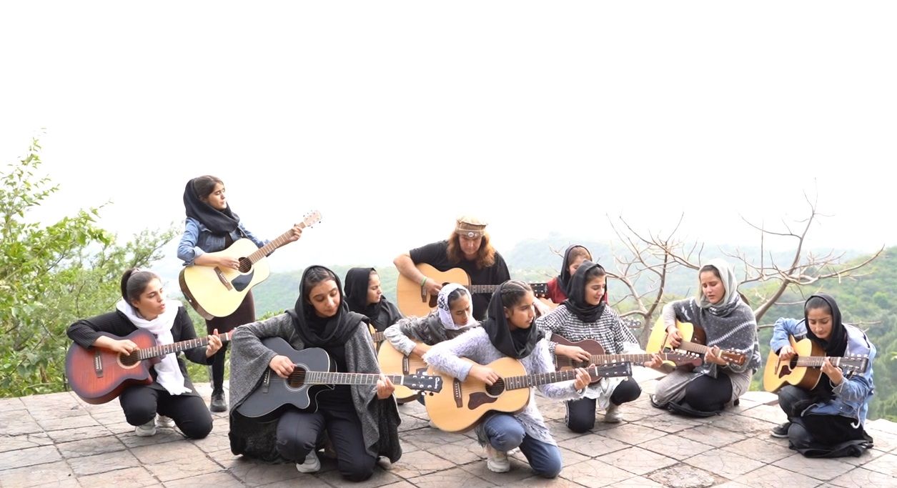 Students of The Miraculous Love Kids playing acoustic guitars together on a hillside in Pakistan, with founder Lanny Cordola